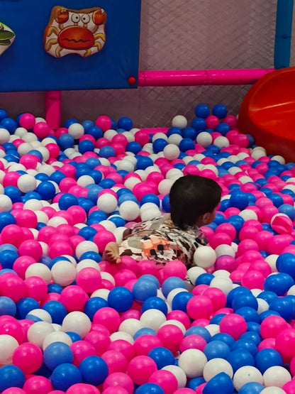 Child playing in a ball pit with pink, blue, and white balls.