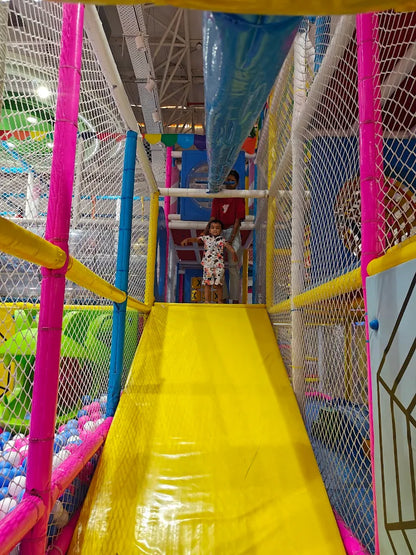 Colorful indoor playground with a yellow slide and pink and blue netting.