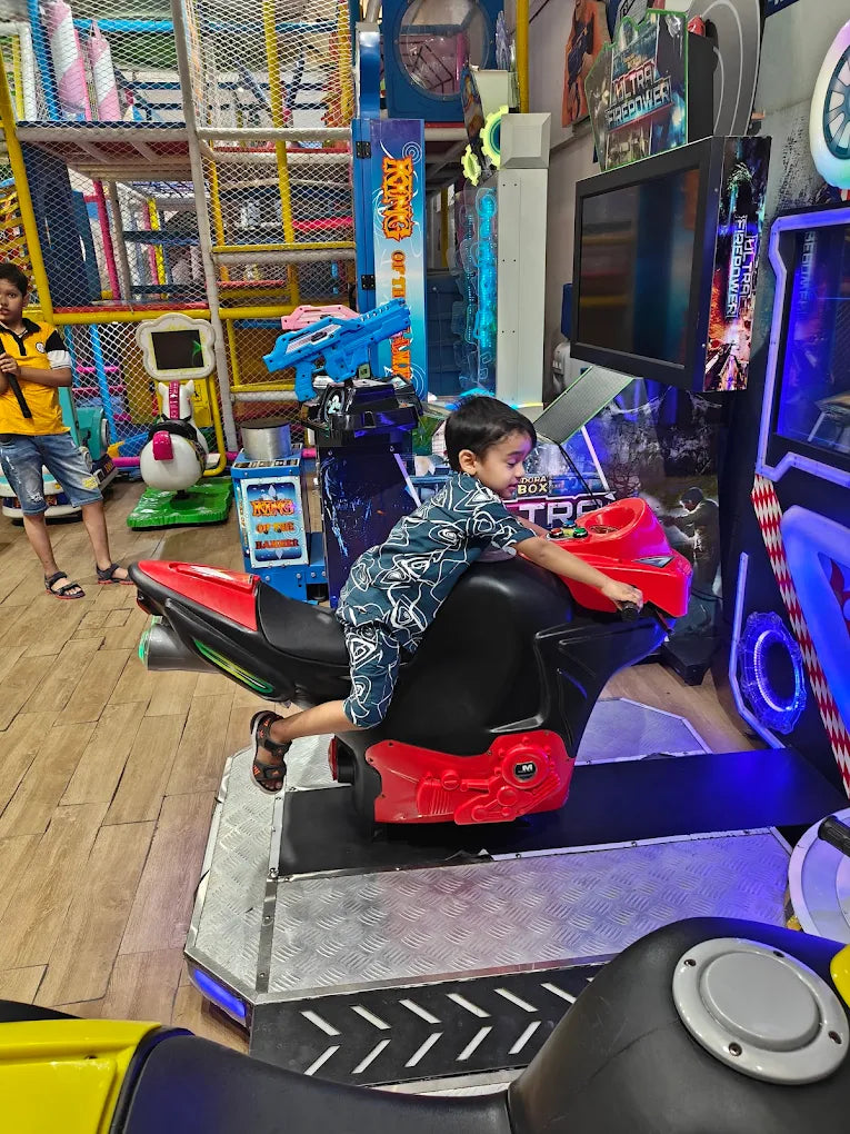 A young boy plays a motorcycle arcade game in an indoor play area.