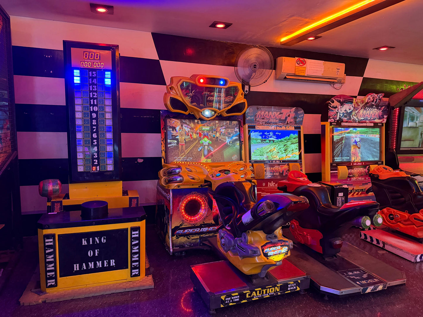 Arcade with motorcycle racing games and a hammer game, lit by neon lights.