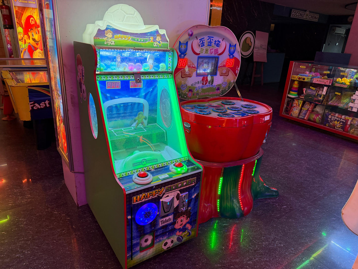 Arcade games, including a soccer-themed game and a "whack-a-mole" style game, are displayed in a dimly lit entertainment venue.