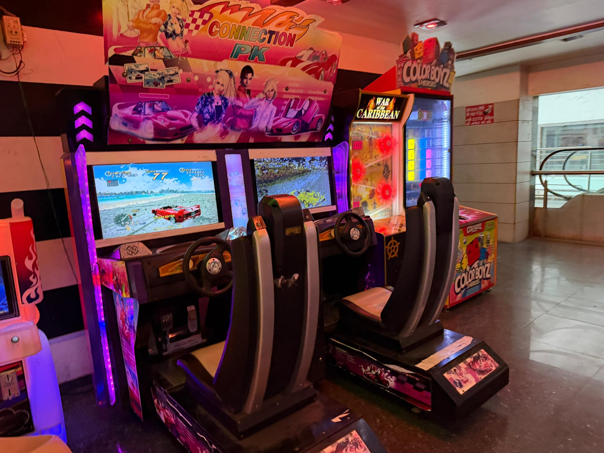 Two racing arcade game cabinets with seats are set up in an arcade. The games feature colorful graphics and racing themes.