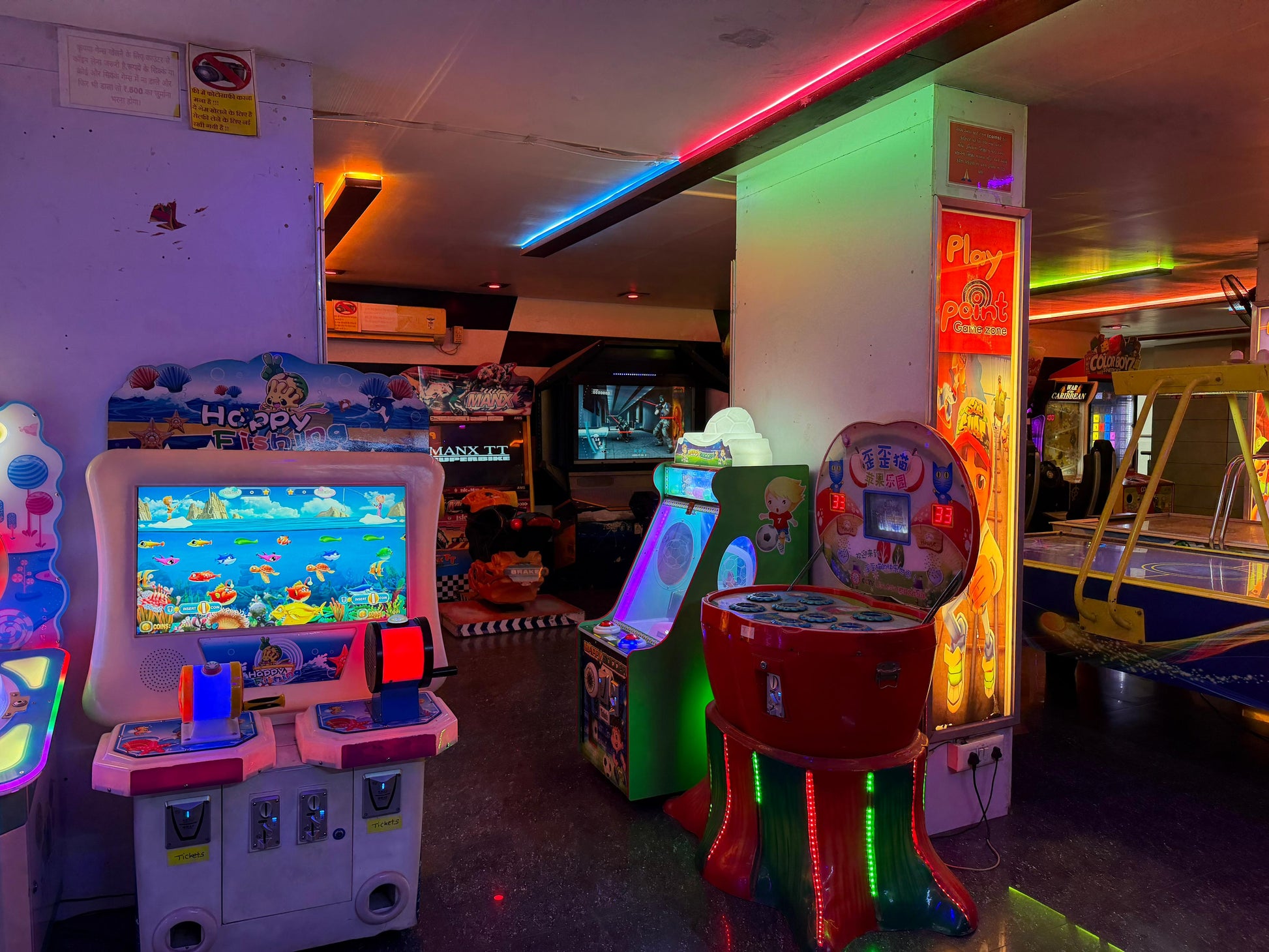 An arcade with colorful lights and various video games, including a fishing game and a motorcycle racing game.
