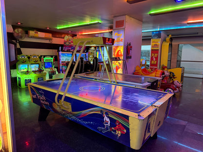 An arcade with air hockey tables and video games, lit by colorful neon lights.
