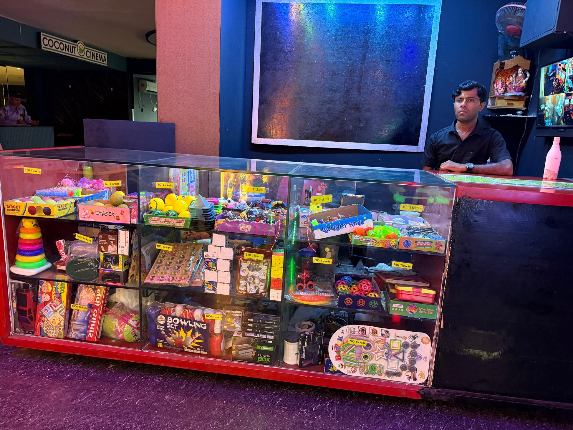 A man stands behind a counter filled with arcade prizes and toys at Coconut Cinema.