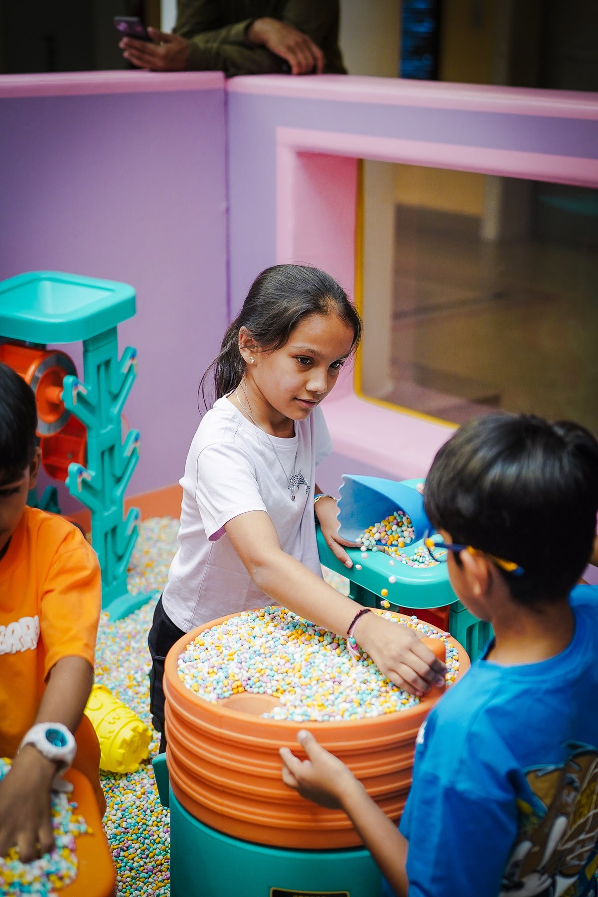 Children play with colorful balls in a ball pit with bright, playful structures.