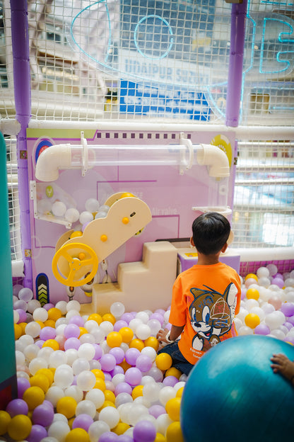 A young boy in an orange shirt plays in a ball pit with a large blue exercise ball.