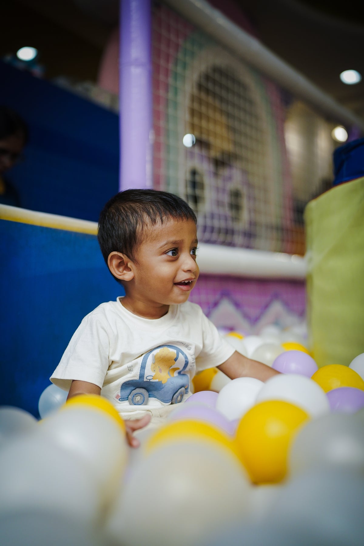 A young boy smiles while playing in a ball pit filled with colorful balls.