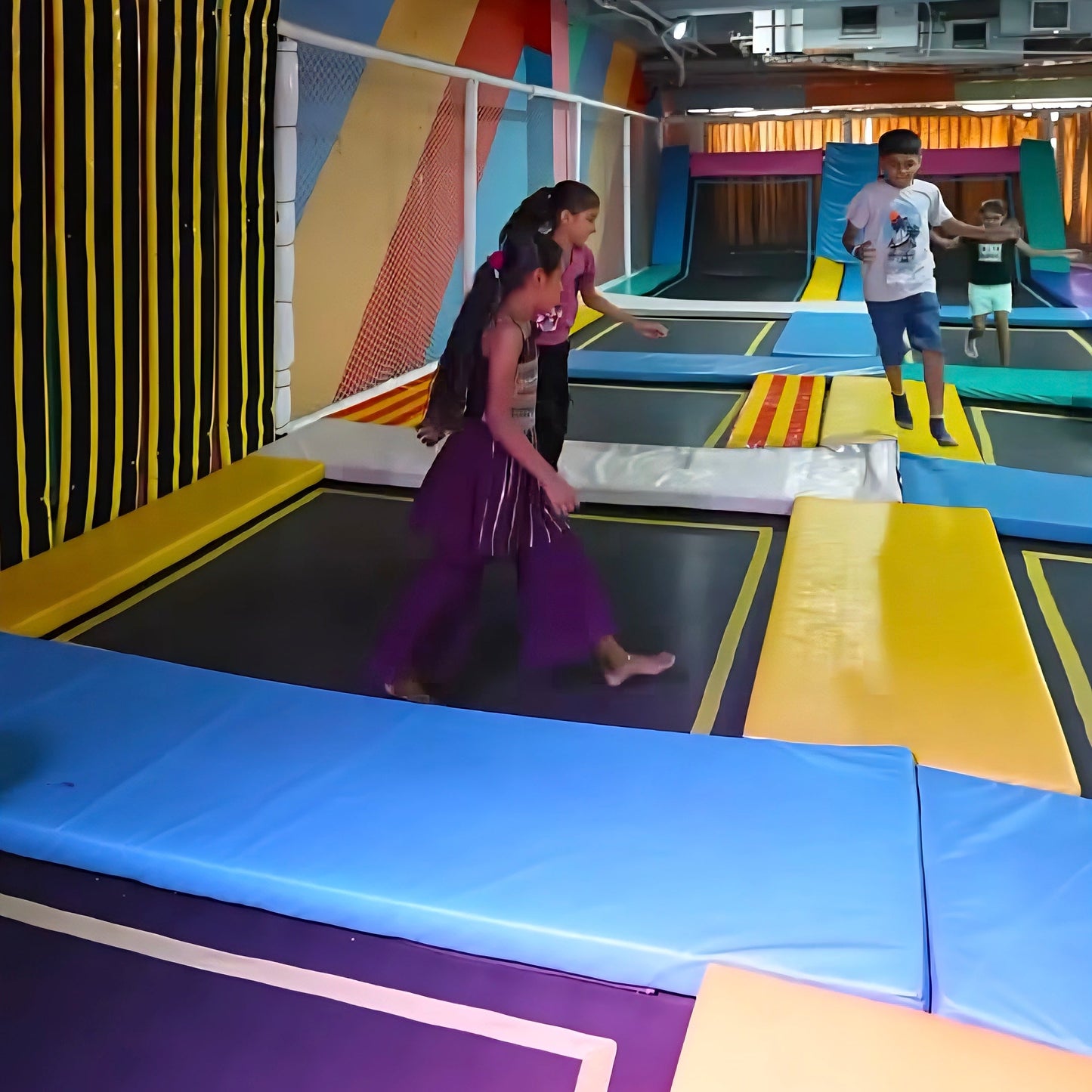 Children jump on trampolines in a colorful indoor play area.