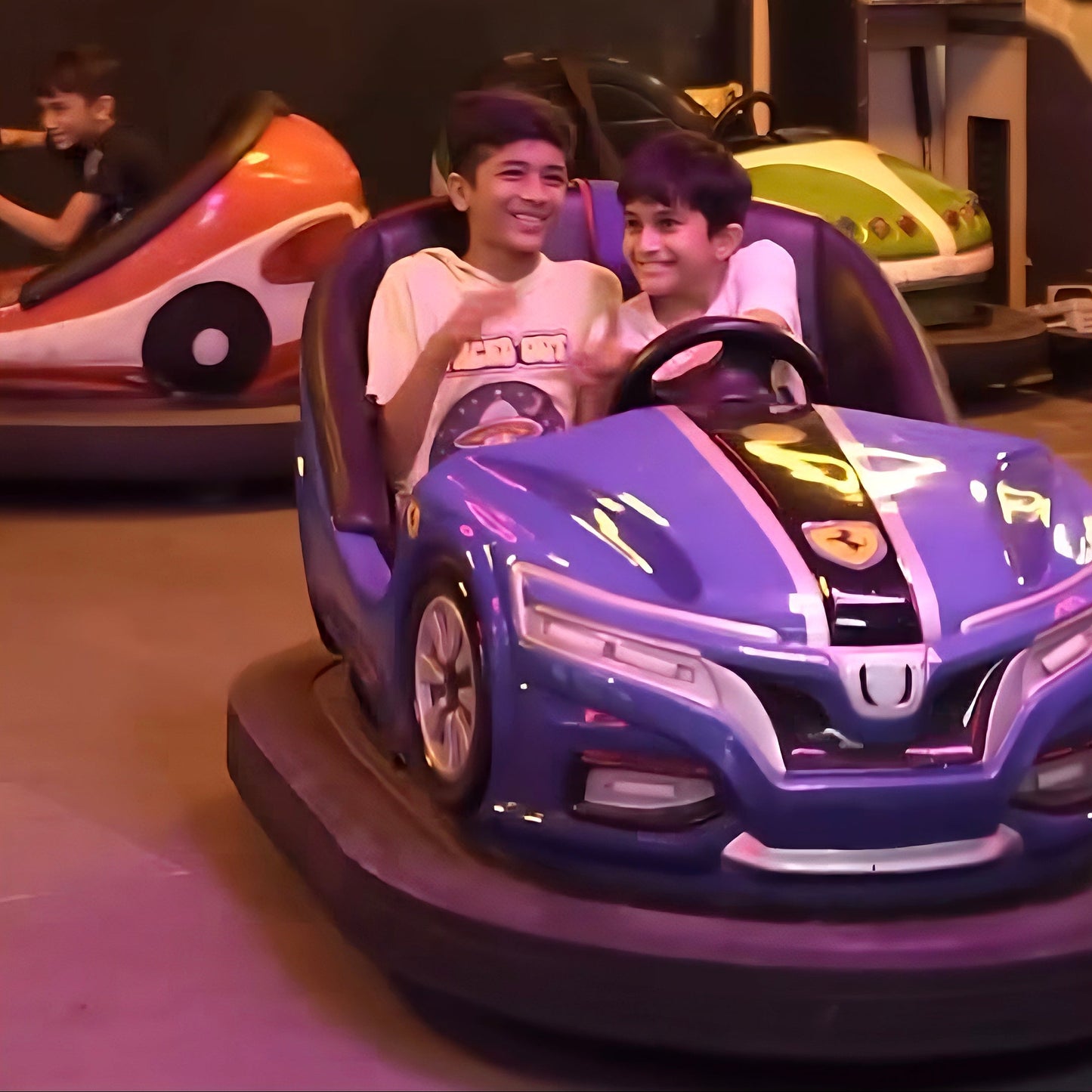 Two young boys smile while riding in bumper cars at an amusement park.
