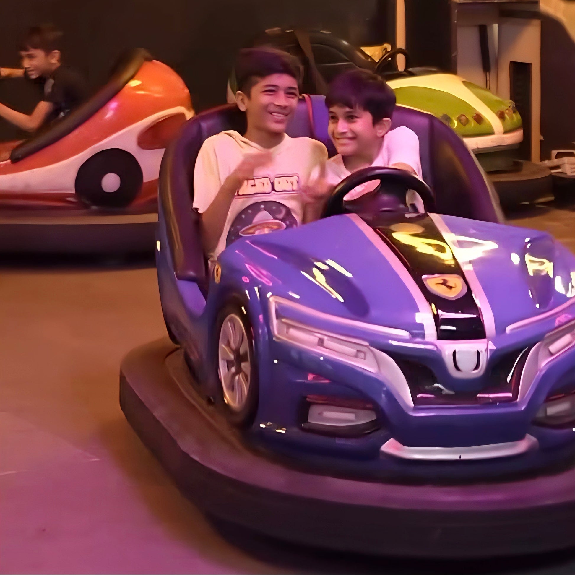 Two young boys smile while riding in bumper cars at an amusement park.