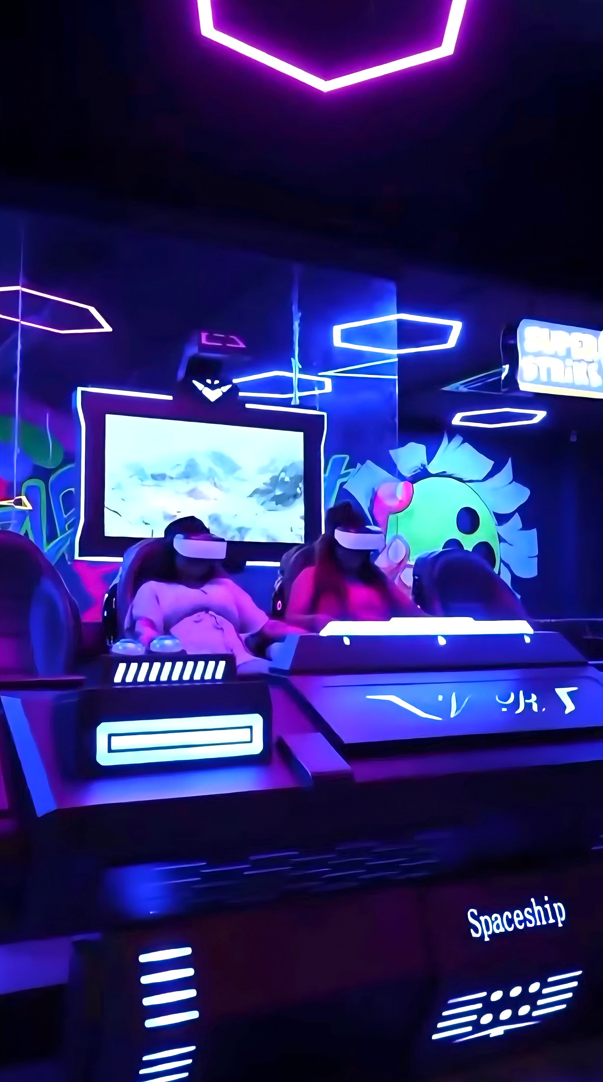 Two young people in VR headsets play a game in a neon-lit arcade.