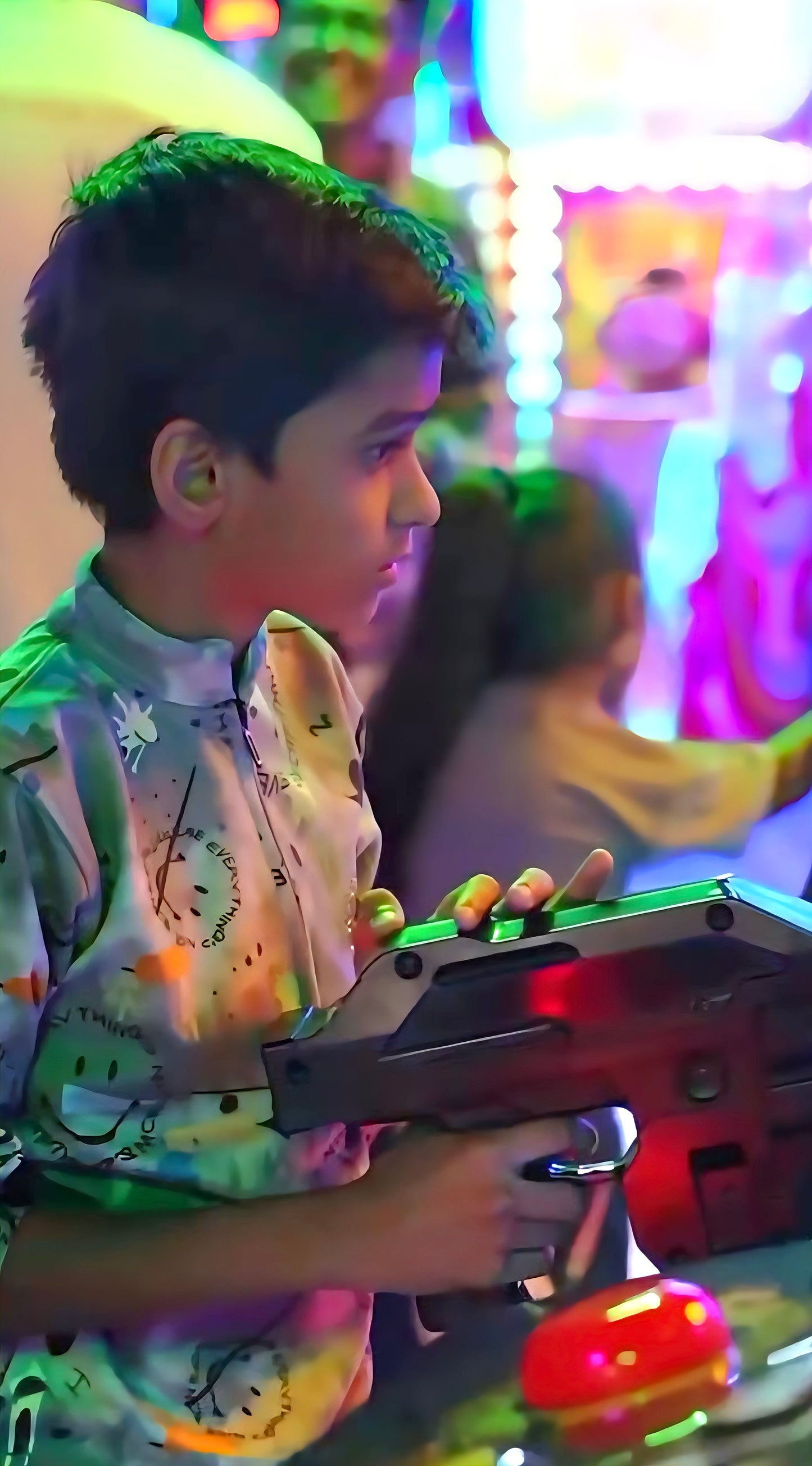 A young boy plays an arcade game with a light gun in a brightly lit arcade.