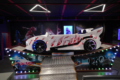 A white race car ride with flame decals and LED lights, likely for children, in an arcade.