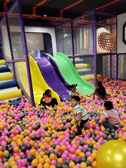 Children play in a ball pit with slides at an indoor playground.