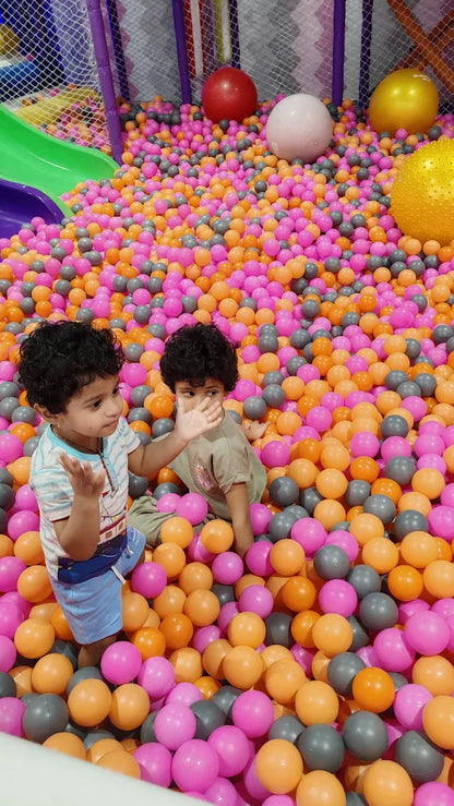 Two young children play in a ball pit filled with pink, orange, and gray balls.