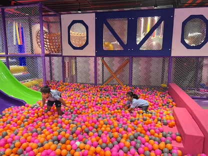 Two young children play in a large ball pit filled with colorful balls at an indoor playground.