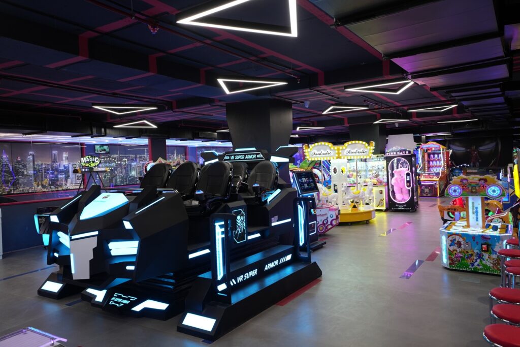 An arcade with VR simulators and various game machines, lit by neon lights.