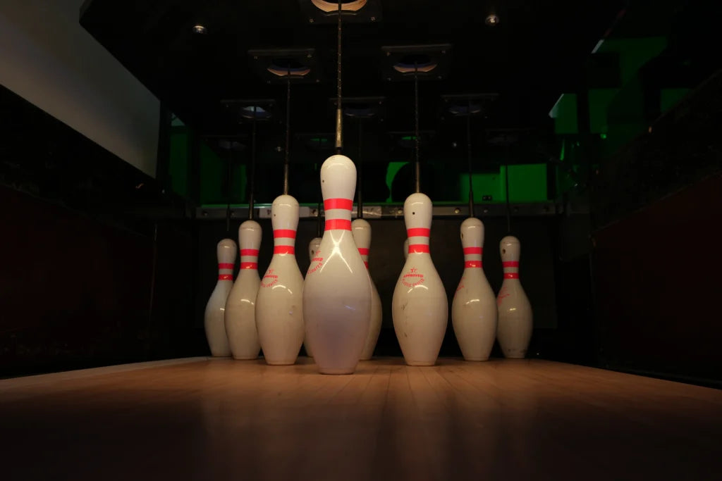 Bowling pins are set up on a wooden lane in a dimly lit bowling alley.