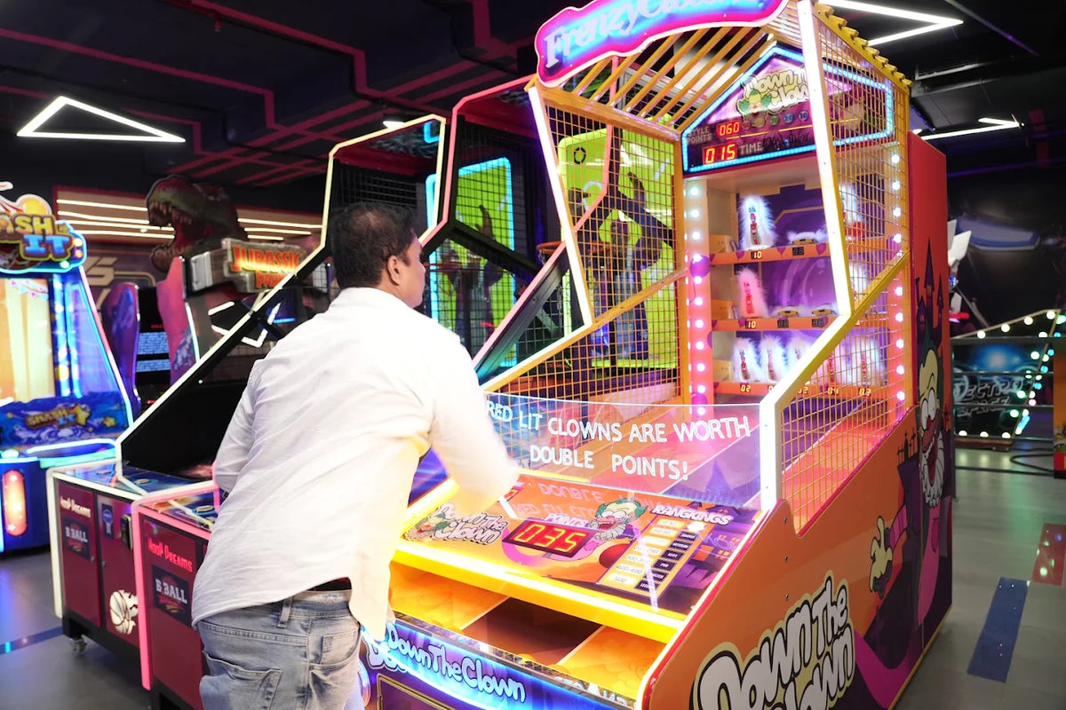 A man plays a "Down the Clown" arcade game in a brightly lit entertainment center.