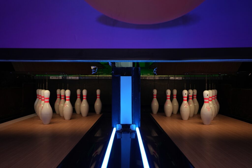 Bowling pins are set up on a wooden lane under purple lighting.