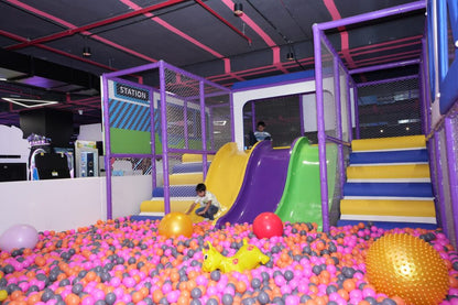 Children play in a colorful ball pit with slides and climbing structures in an indoor playground.