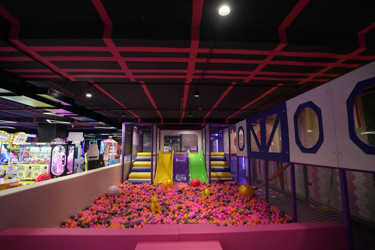 A colorful ball pit with slides and arcade games in an indoor play area for children.