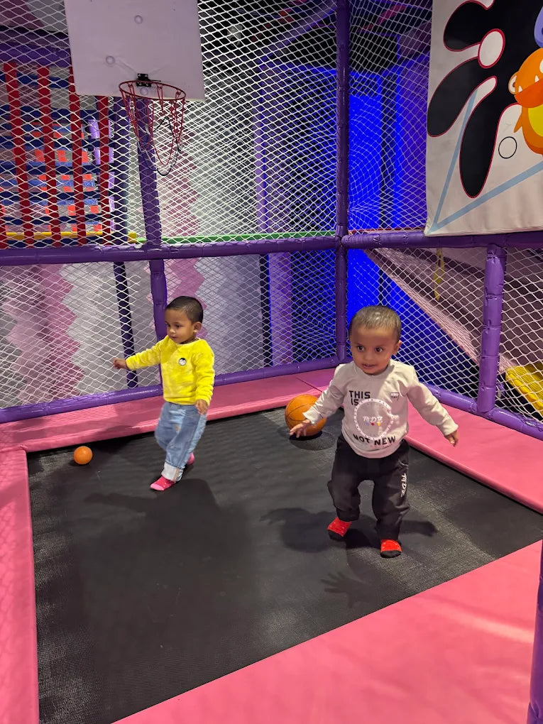 Two toddlers play on a trampoline in an indoor play area.