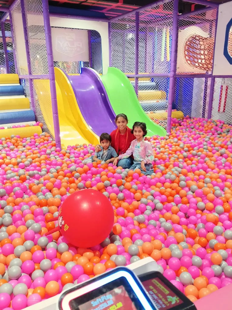 A family with young children poses in a colorful ball pit with slides in the background.