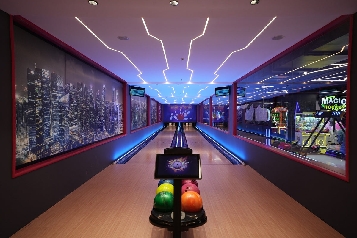 A modern bowling alley with neon lights and city skyline murals, featuring a ball return with colorful bowling balls.