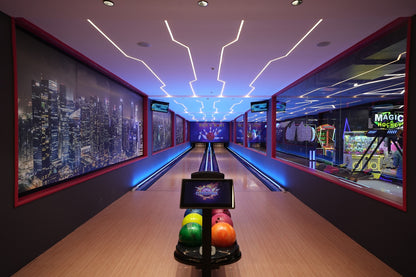 A modern bowling alley with neon lights and city skyline murals, featuring a ball return with colorful bowling balls.