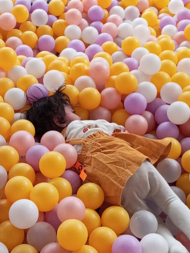 A young child lies in a ball pit filled with colorful balls.