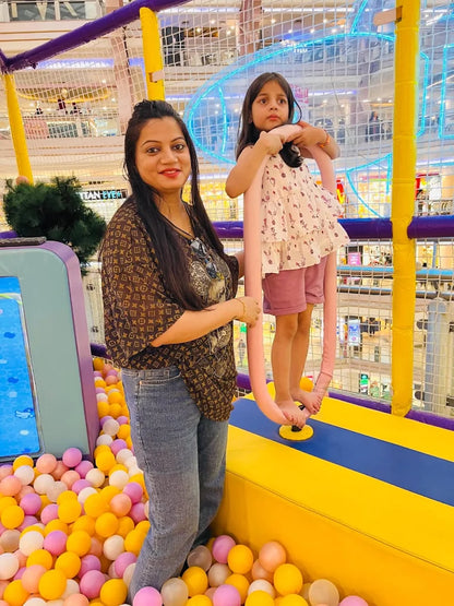 A woman and a young girl in a colorful indoor playground with a ball pit.