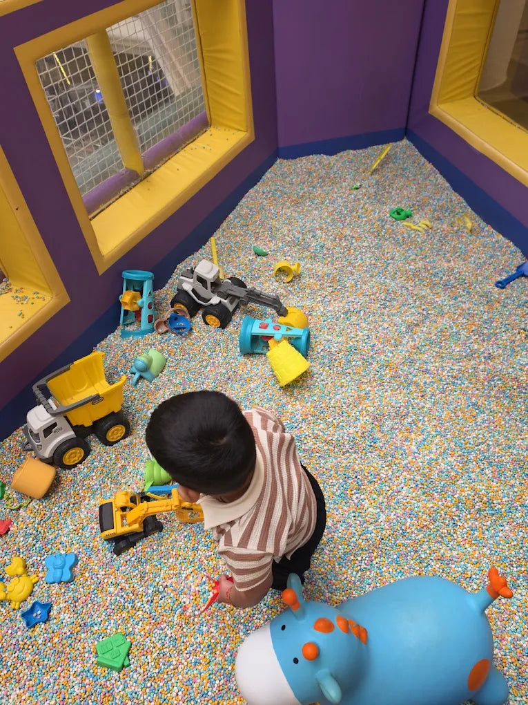 A young child plays with toy construction vehicles in a ball pit filled with colorful balls.