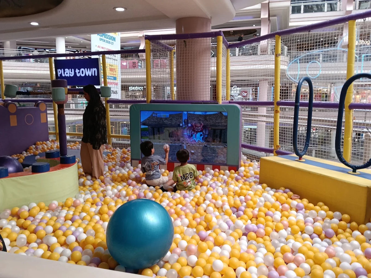 Children play in a ball pit at an indoor playground, with a woman watching.