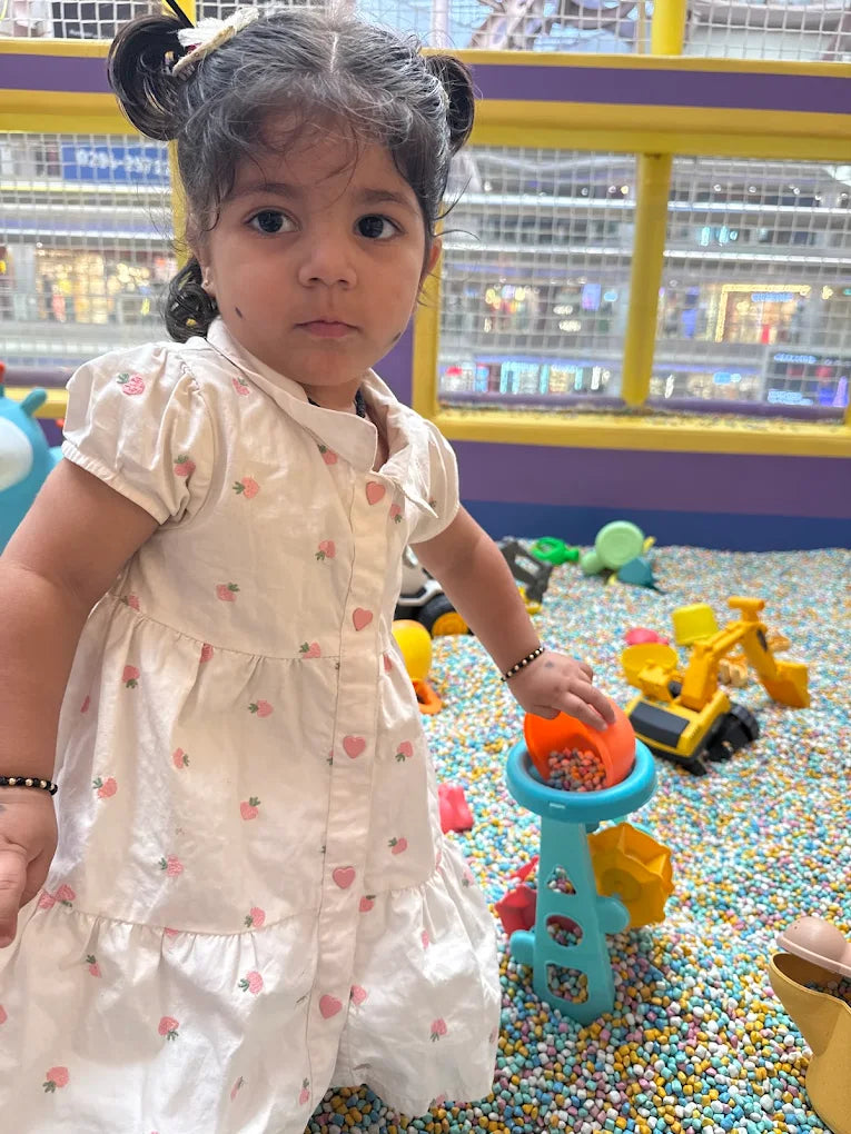 A young girl plays with colorful toys in a ball pit.