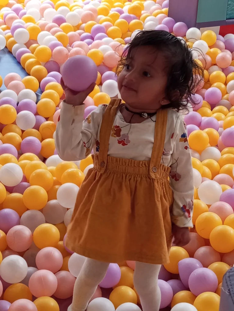A young child plays in a ball pit, holding a purple ball.