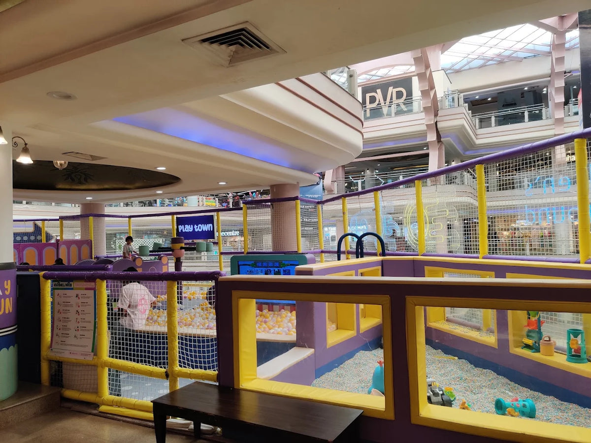A colorful indoor playground with children playing in a ball pit and a soft play area.