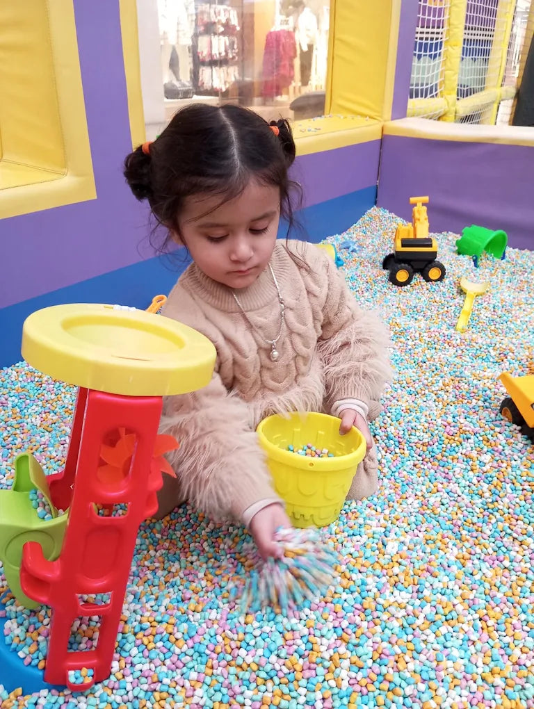 A young child plays in a ball pit with colorful balls and toys.