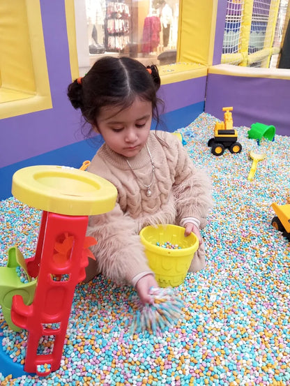 A young child plays in a ball pit with colorful balls and toys.