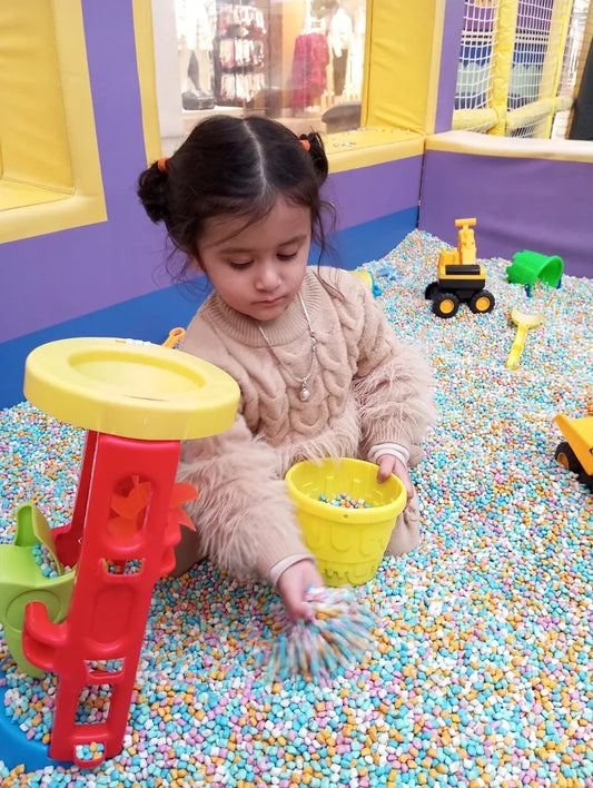 A young child plays in a ball pit with colorful balls and toys.