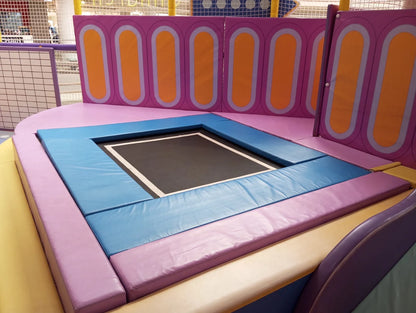A colorful indoor trampoline area with padded walls and a black trampoline mat.