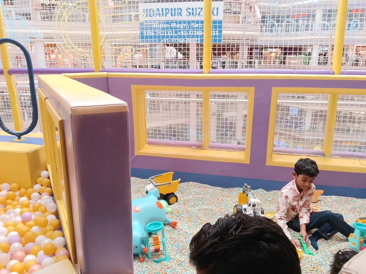 A young boy plays in a ball pit with toys, while other children are partially visible.