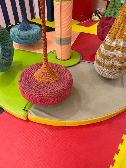 Colorful, crocheted hanging seats and soft play mats in a children's play area.