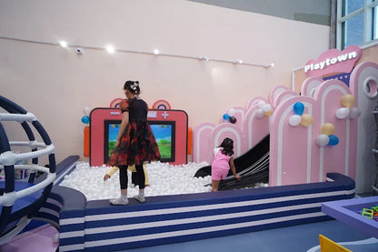 Children play in a ball pit and on a slide at a colorful indoor playground.