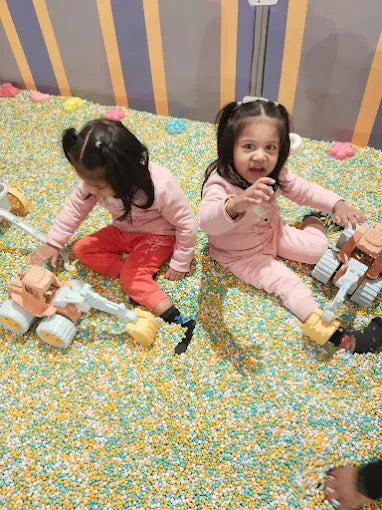 Two young children play with toy construction vehicles in a ball pit filled with colorful balls.
