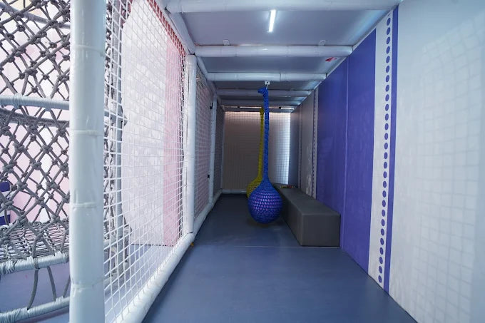 Indoor play area with rope nets, hanging balls, and padded walls.