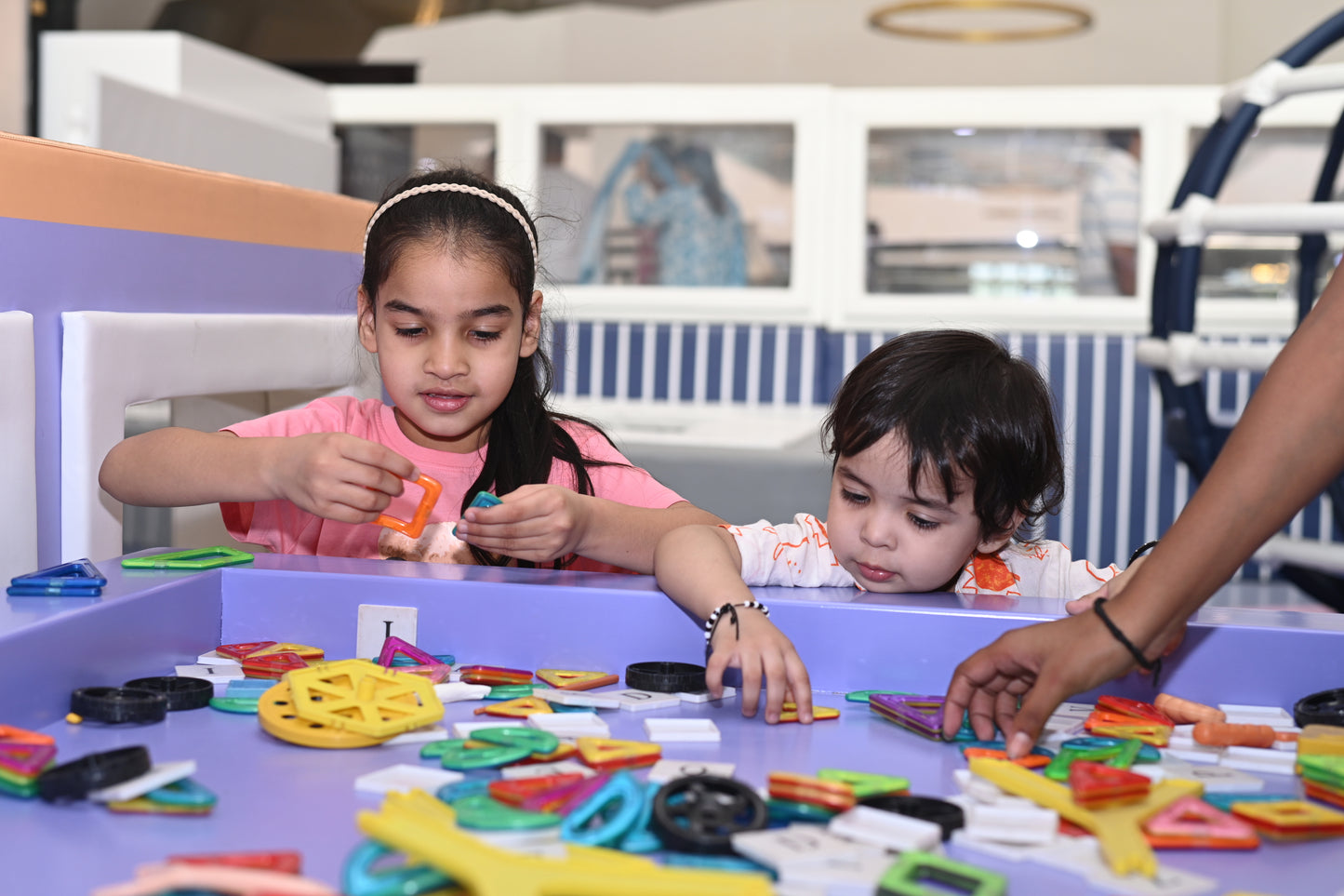 Two young children play with colorful magnetic building toys at a purple table.