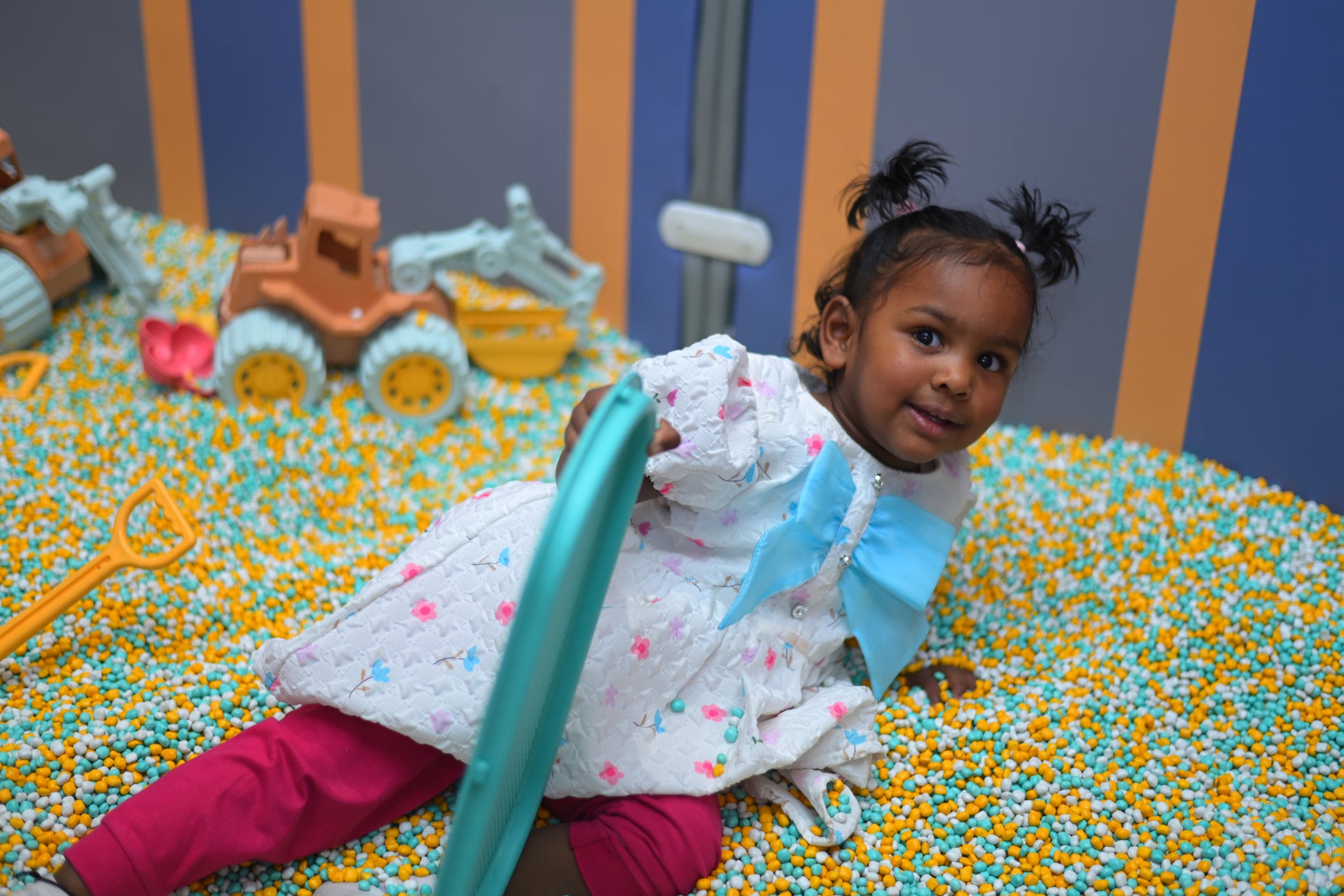 A young girl plays in a ball pit with toy construction vehicles.