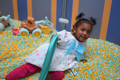 A young girl plays in a ball pit with toy construction vehicles.